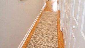 A hallway with a wooden floor, a rug, and a framed picture on the wall.