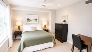 Quarto com cama, luminárias de cabeceira, cômoda, escrivaninha e cadeira.