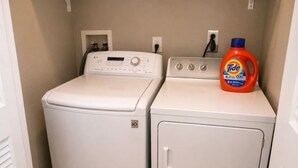 A laundry room with two white washing machines and a Tide detergent bottle.