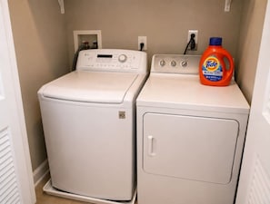 A laundry room with two white washing machines and a Tide detergent bottle.