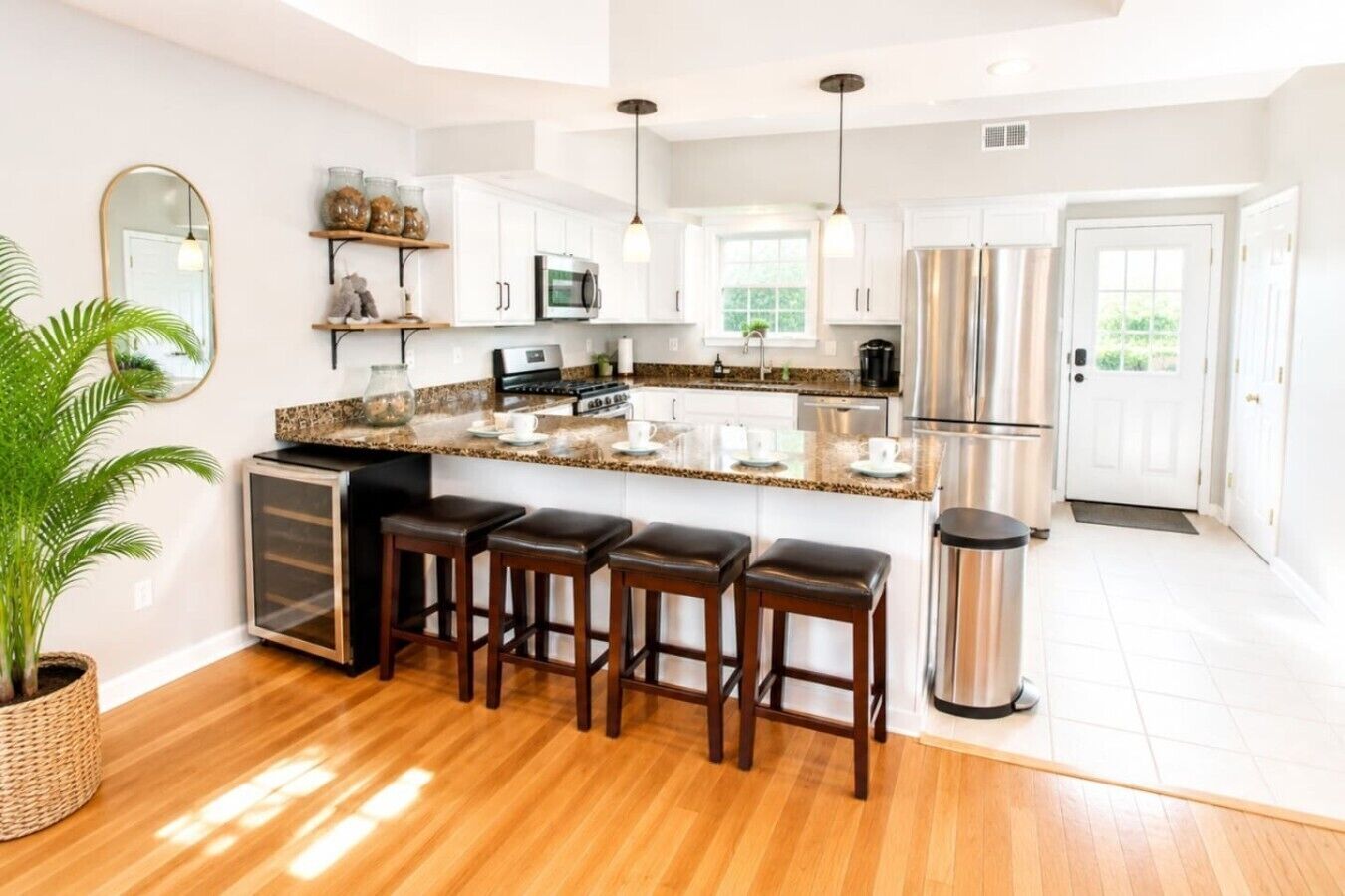A modern kitchen with white cabinets, a granite countertop, a stainless steel refrigerator, and a bar area with stools.