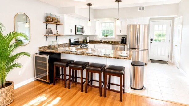 A modern kitchen with white cabinets, a granite countertop, a stainless steel refrigerator, and a bar area with stools.