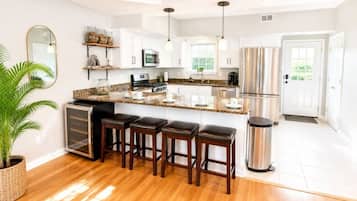 A modern kitchen with white cabinets, a granite countertop, a stainless steel refrigerator, and a bar area with stools.