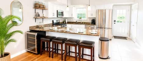 A modern kitchen with white cabinets, a granite countertop, a stainless steel refrigerator, and a bar area with stools.