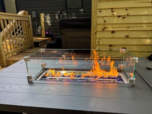 En eldstad med glasväggar och en metallram, placerad på ett trädäck.