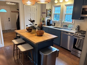 A modern kitchen with a central island, bar stools, a dishwasher, a stove, and a coffee station.