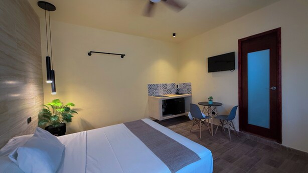 Een hotelkamer met een bed, een eettafel met stoelen, een plafondventilator, een aan de muur bevestigde televisie en een deur.
