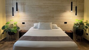Een moderne hotelkamer met een groot bed, twee nachtkastjes, een wandairconditioner en twee hanglampen.