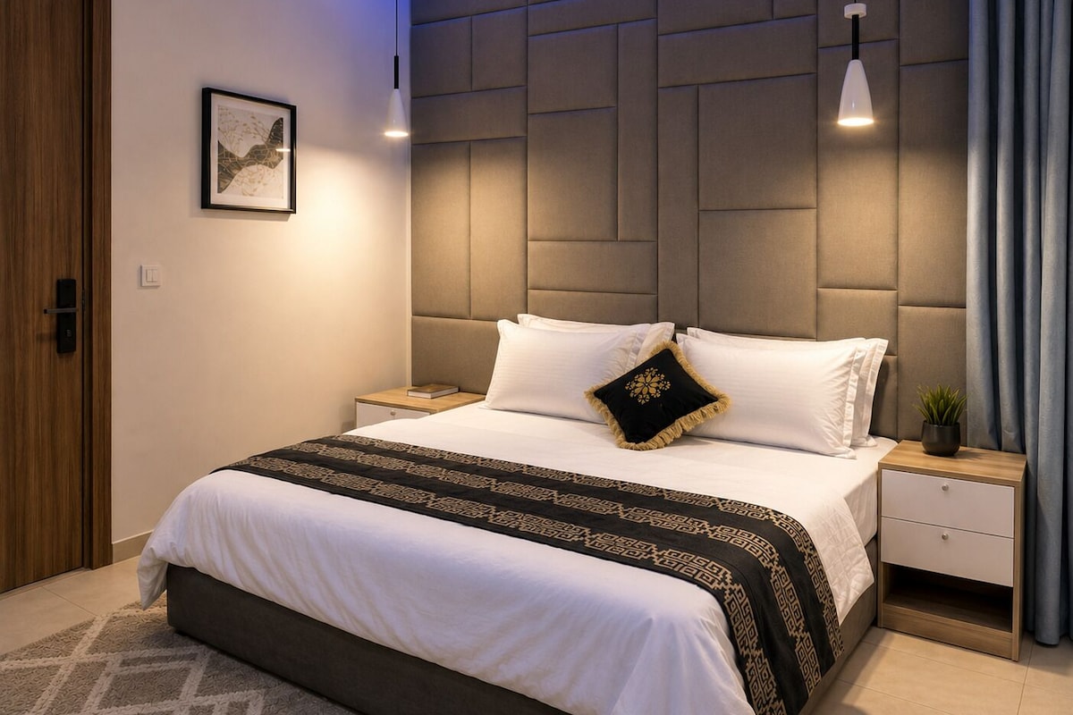 A modern bedroom with a large bed, a headboard with a geometric pattern, bedside tables with lamps, and a framed picture on the wall.