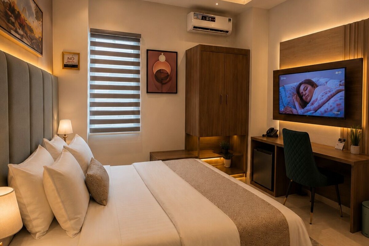 A modern hotel room with a large bed, a desk, a television, and an air conditioning unit.