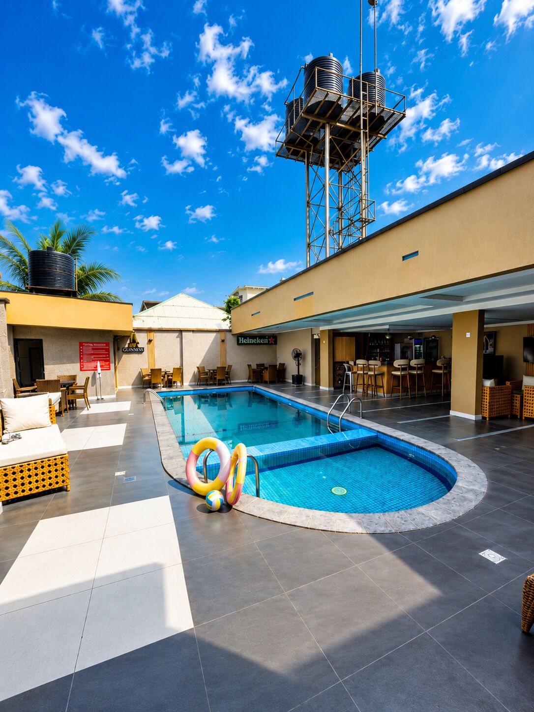 Un espace piscine comprenant un château d’eau, des fauteuils et un bar.