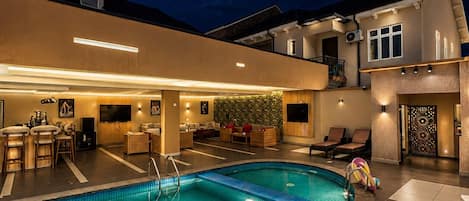 A swimming pool with a bar area, lounge chairs, and a covered seating area.
