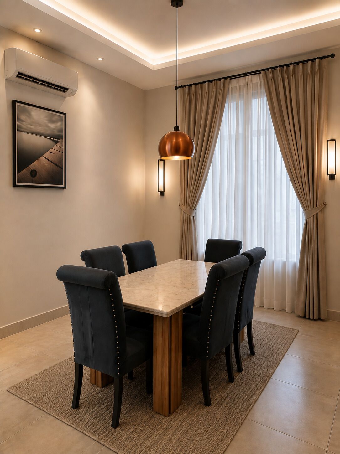 Un coin repas avec une table rectangulaire entourée de chaises, un luminaire suspendu, un appareil de climatisation, un tableau encadré au mur et une fenêtre avec des rideaux.