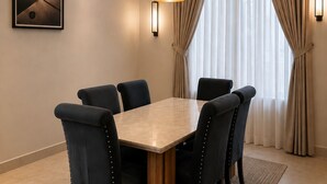 A dining area with a rectangular table surrounded by chairs, a pendant light, an air conditioning unit, a framed picture on the wall, and a window with curtains. - Kiniz Apartments and Hotel Uyo (Uyo)