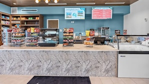 Un bar con scaffali pieni di patatine e snack, una vetrina refrigerata e un cartellone con la scritta 'Breeze Canteen' e 'Volleyball Court'.
