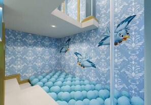 Ein Kinderspielbereich mit Bällebad und Wandgemälden von Vögeln.