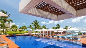 A swimming pool with sun loungers and umbrellas, surrounded by palm trees and a clear sky. - 2BR Apartment with Beach Club (Cancún)
