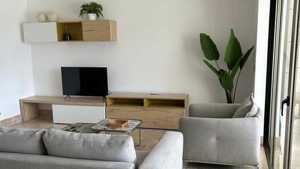 A modern living room with a sofa, two armchairs, a coffee table, a flat-screen TV, and a wooden entertainment unit with a plant. - 2BR Apartment with Beach Club (Cancún)