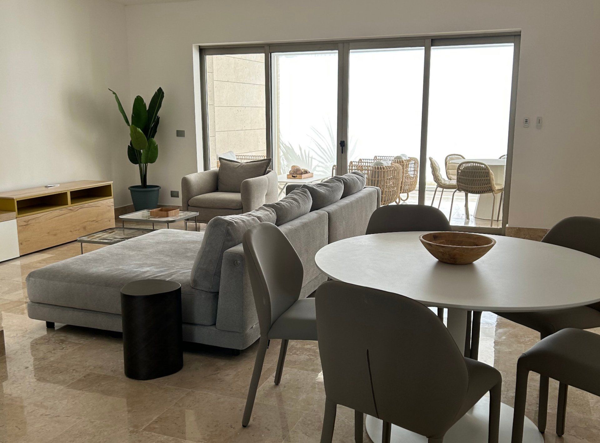 A modern living room with a sofa, chairs, a dining table, and a large window.