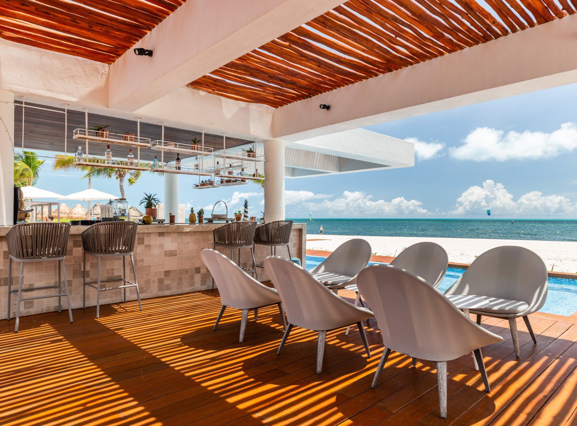 An outdoor bar area with a view of the ocean, wooden flooring, and modern bar stools.