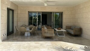 A modern patio with a dining table and chairs, a sofa, and a ceiling fan. - 2BR Apartment with Beach Club (Cancún)