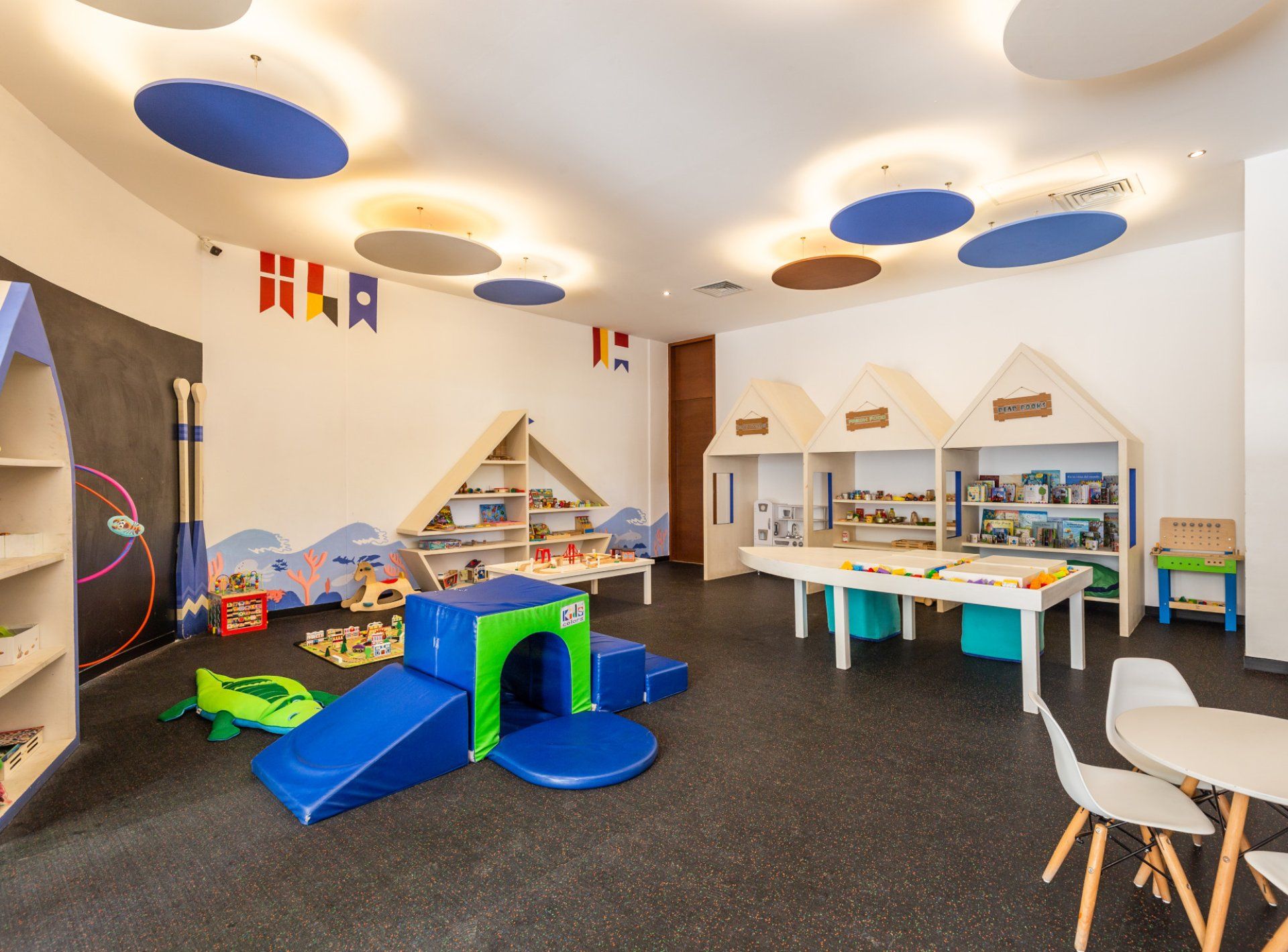 Uma área de recreação infantil com escorrega, mesas de brinquedo e prateleiras para guardar.