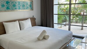 A hotel room with a large bed, a window with a view of greenery, and a painting on the wall. - 2BR Apartment with Beach Club (Cancún)