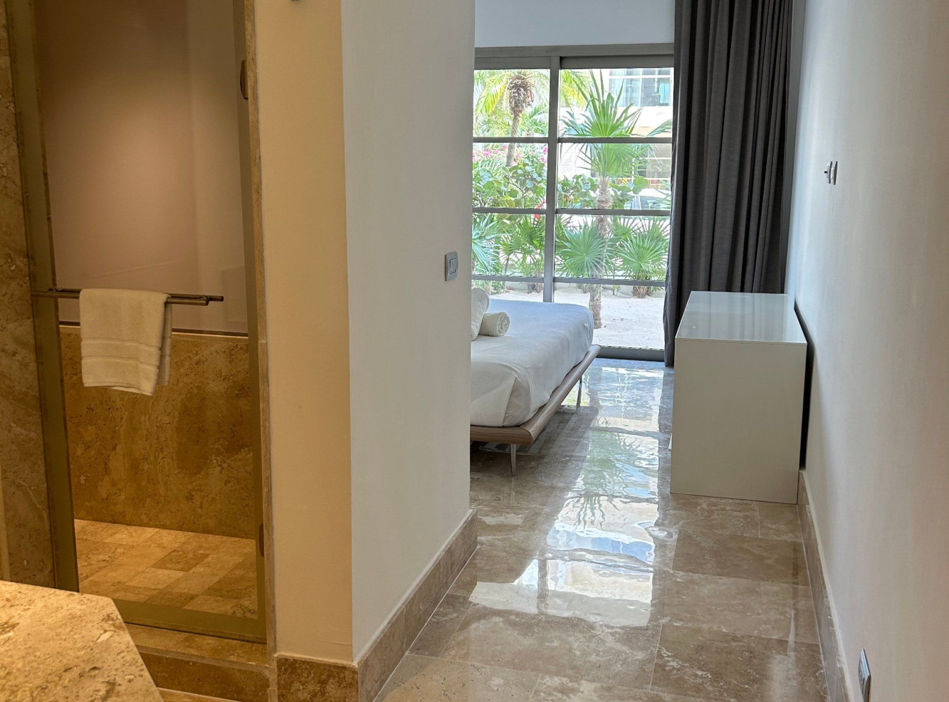 Quarto de hotel com cama, uma mesinha e zona de chuveiro.