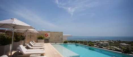 A poolside area with lounge chairs and umbrellas, a lifebuoy, and a view of the ocean.