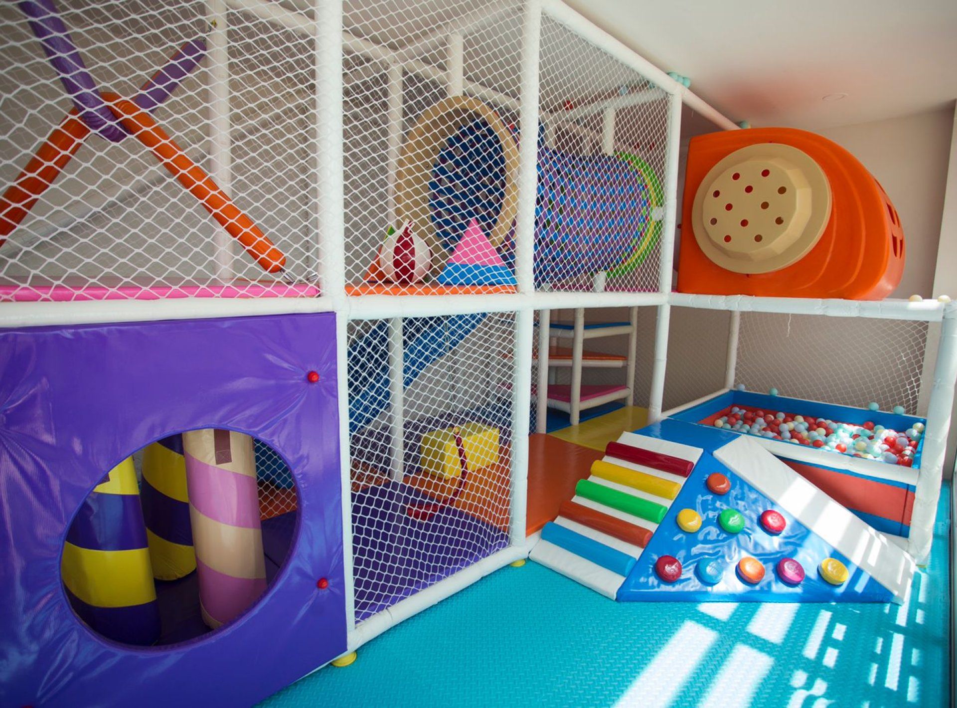 Ein Kinderspielbereich mit Rutsche, Kletternetz und Bällebad.