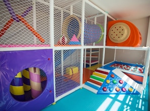 Un área de juegos infantiles con tobogán, red de escalada y piscina de pelotas.