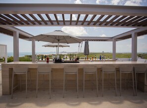 Un espace bar extérieur avec vue sur l’océan, agrémenté d’une pergola et de parasols.