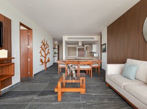 Un salon moderne avec un canapé, une table à manger et des chaises, une sculpture en bois décorative et, au fond, un coin cuisine.