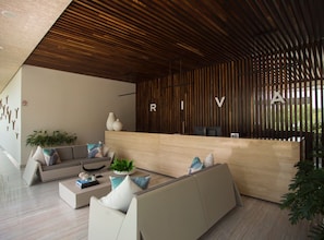 Una moderna zona de recepción con techo de listones de madera, una mesa de recepción y un área de estar con sofás y una mesa de centro.