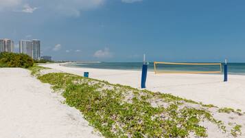 Ein Beachvolleyballfeld mit Netz, umgeben von Sand und vereinzelter Vegetation.
