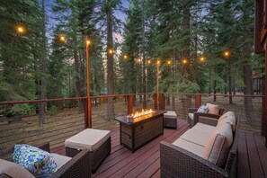 Een terras buiten met rieten meubilair, een vuurplaats en lichtjes.
