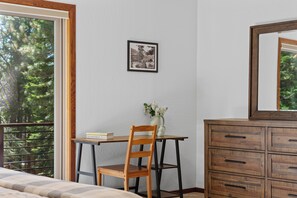 Et soveværelse med seng, skrivebord med stol, kommode, et billede i ramme på væggen og en balkon med gelænder.