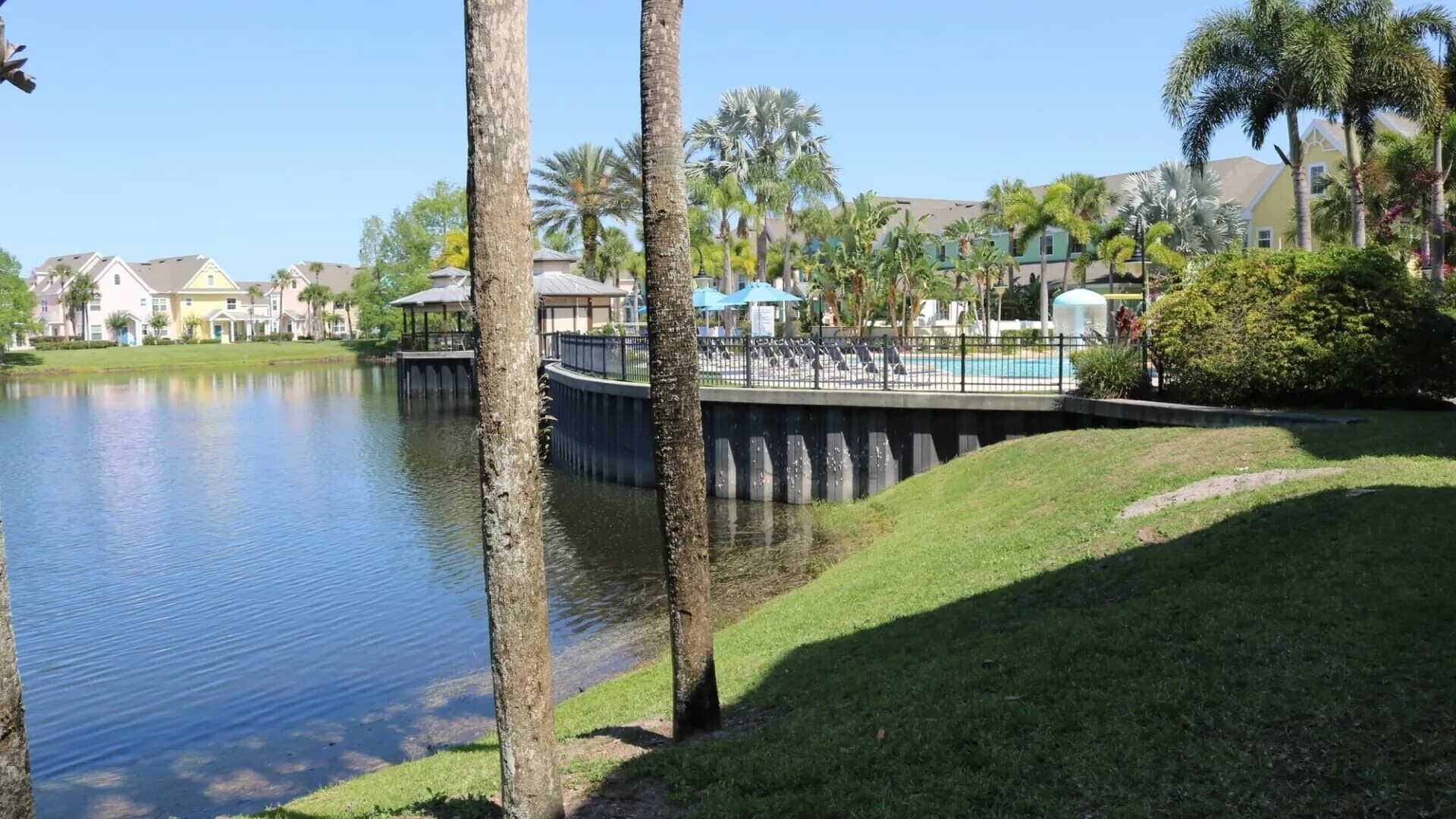 A calm lake with a dock, surrounded by greenery and residential buildings.