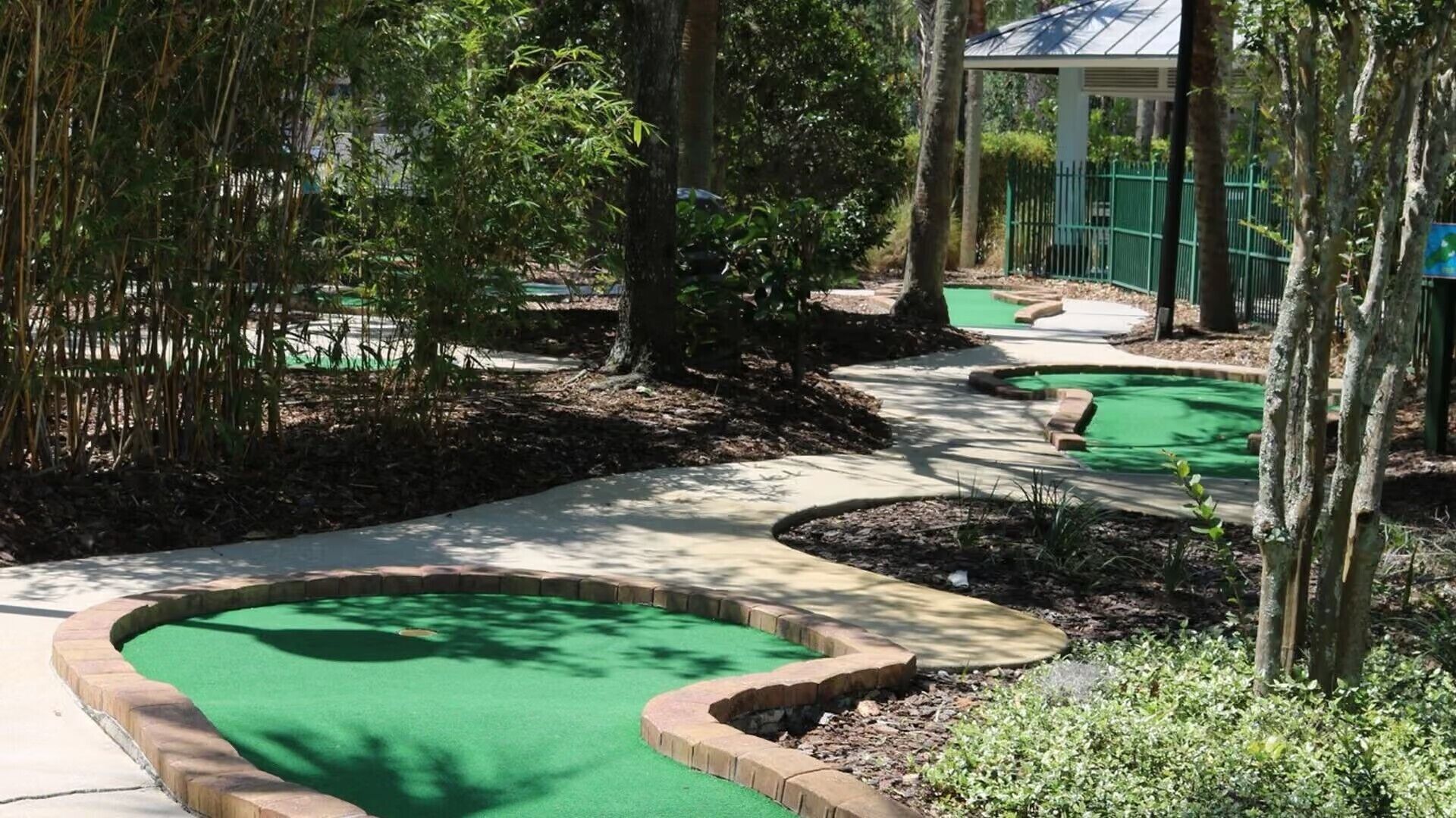 Un campo de mini golf con varias áreas de juego verdes, rodeado de árboles y un pabellón cubierto.