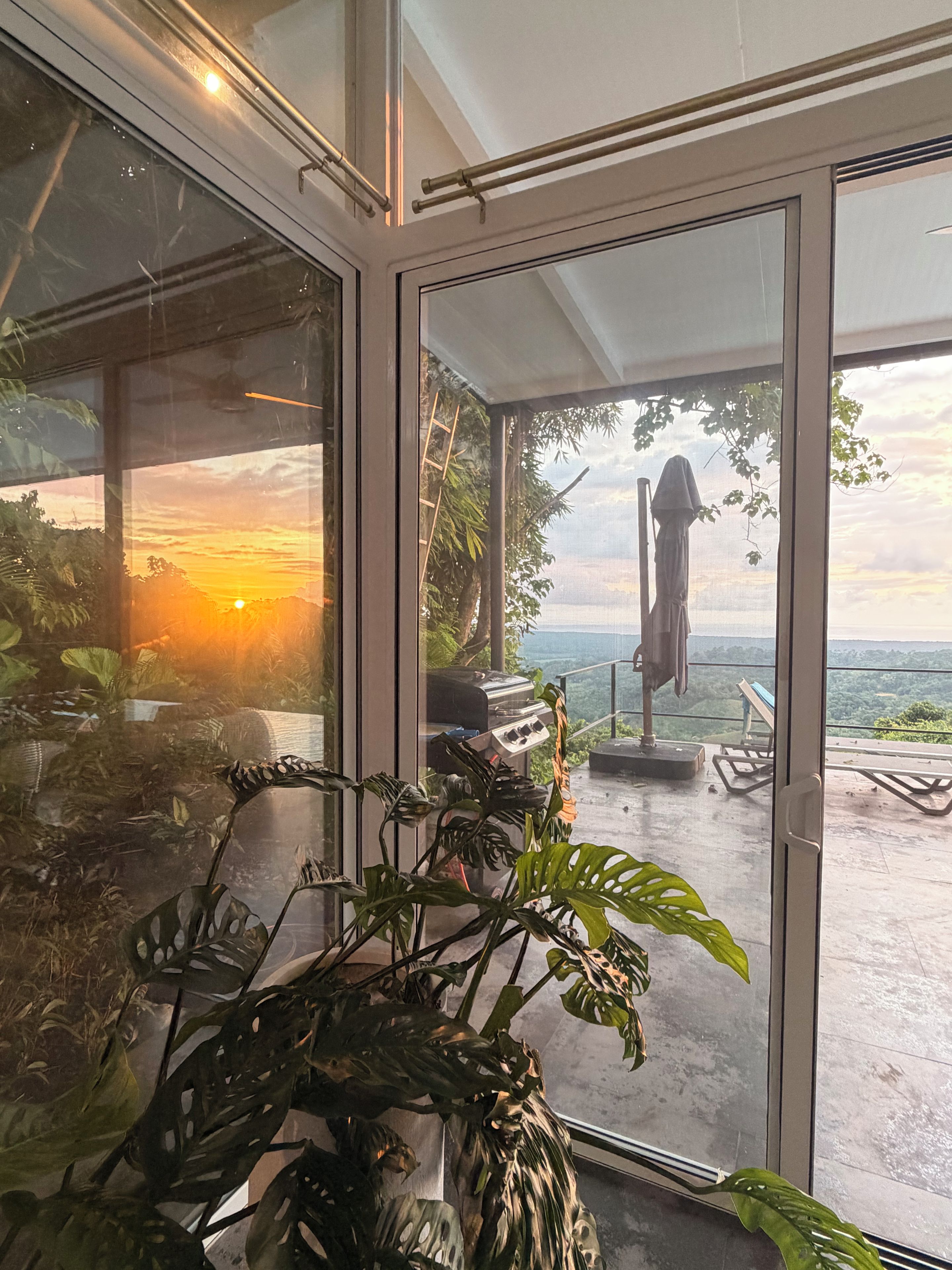 Interior moderno com vista para o pôr do sol sobre a água, uma churrasqueira e área de estar ao ar livre.