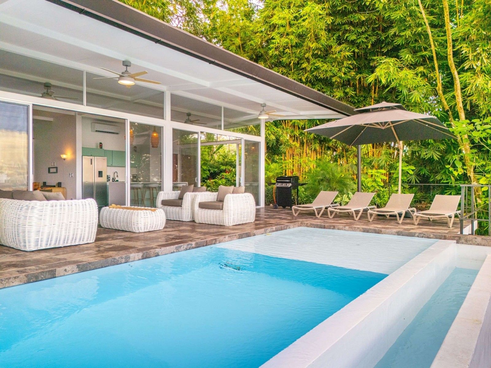 Ein moderner Poolbereich im Freien mit Liegestühlen, einer überdachten Lounge und Blick auf üppiges Grün.