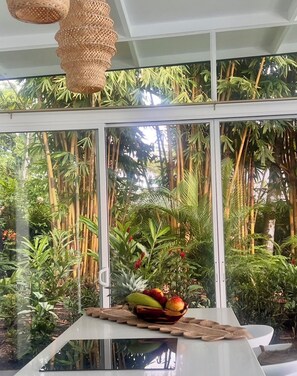 A room with a large window, a white table, and a woven basket with fruits.