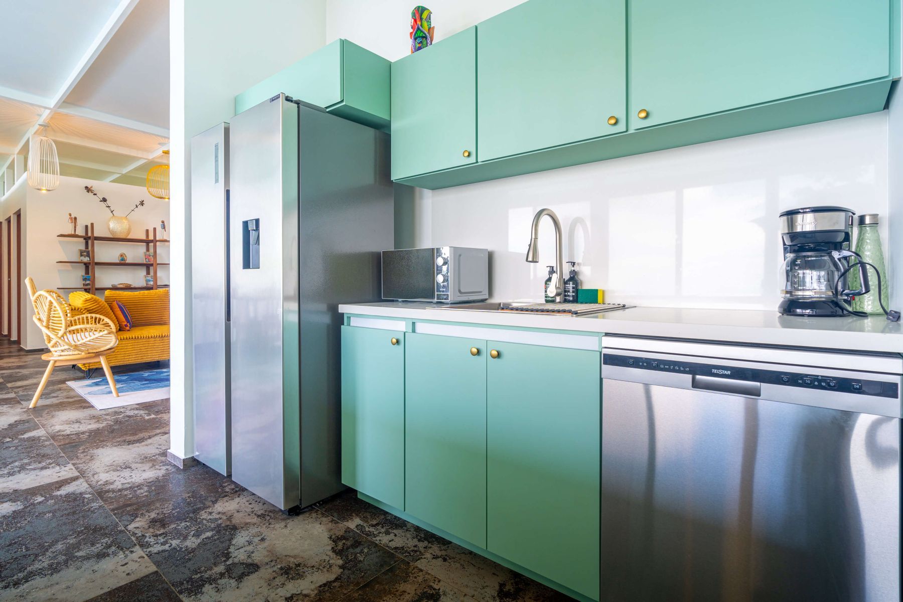 Een keuken met blauwgroene kastjes, een roestvrijstalen koelkast, een magnetron, een koffiezetapparaat en een vaatwasser.