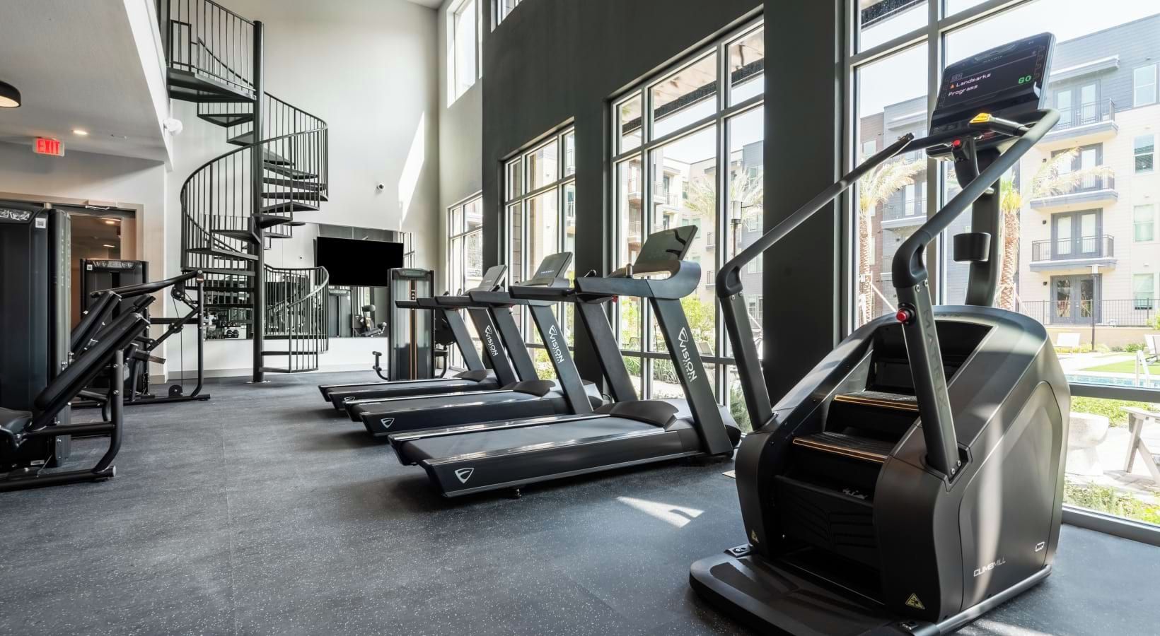 A gym with treadmills, a TV, and a staircase.