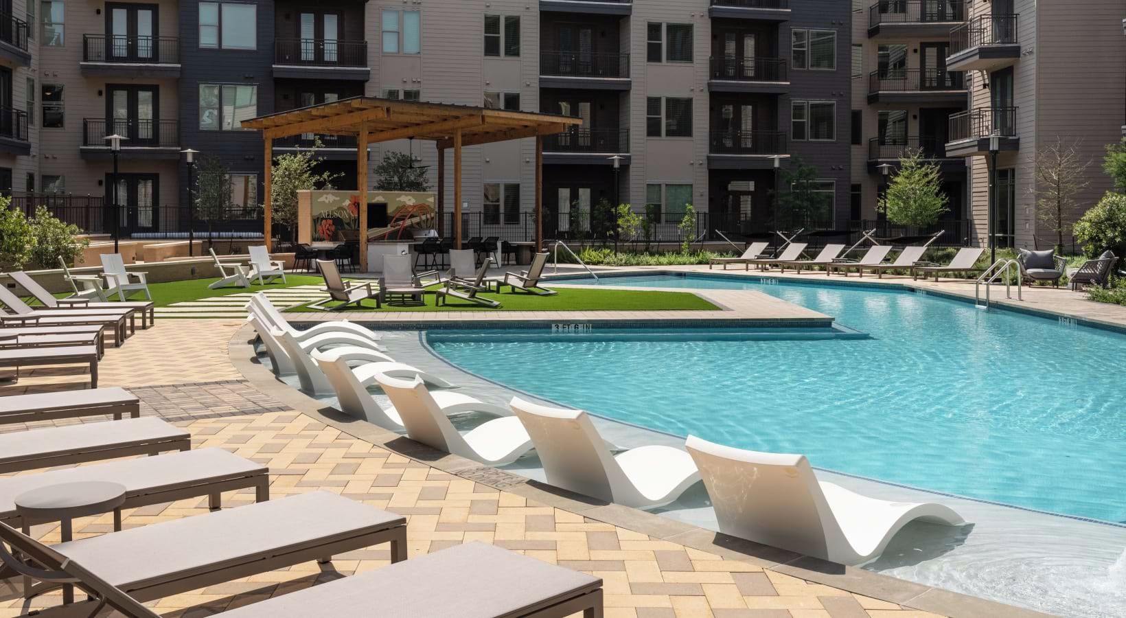 A swimming pool with lounge chairs and a pergola, surrounded by apartment buildings.