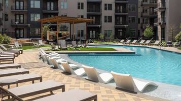 A swimming pool with lounge chairs and a pergola, surrounded by apartment buildings.