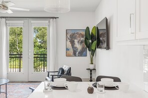 Ein Essbereich mit einem Tisch für zwei Personen, einem Deckenventilator und einem großen Fenster mit Blick auf viel Grün.