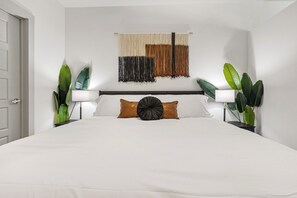 Ein Hotelzimmer mit einem großen Bett, zwei Nachttischlampen, einer Wandweberei und Topfpflanzen.