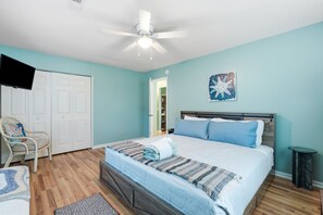 Een slaapkamer met een bed, een stoel, een plafondventilator en een deur.