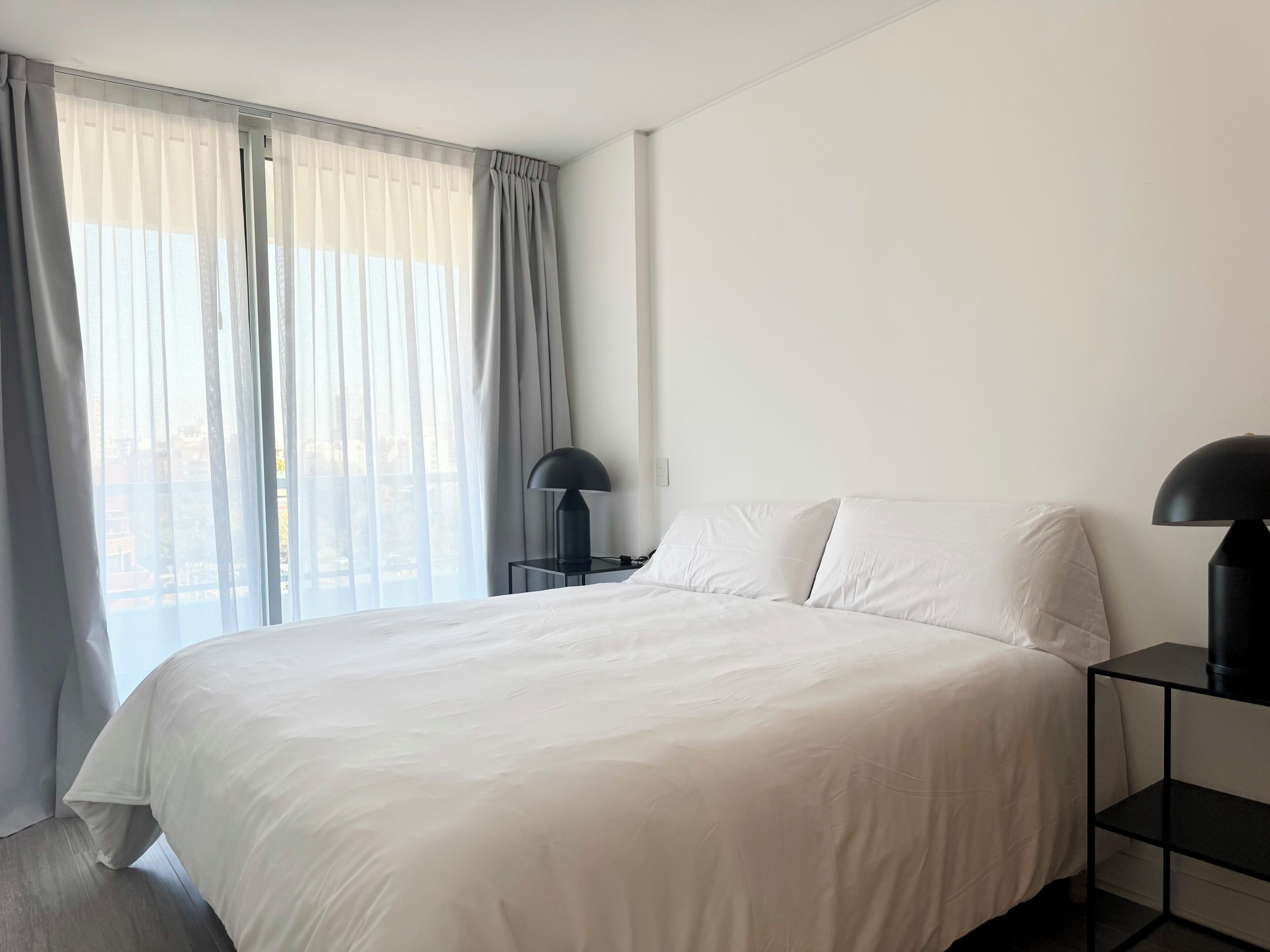 Une chambre à coucher avec un grand lit, deux tables de chevet et une fenêtre avec des rideaux.